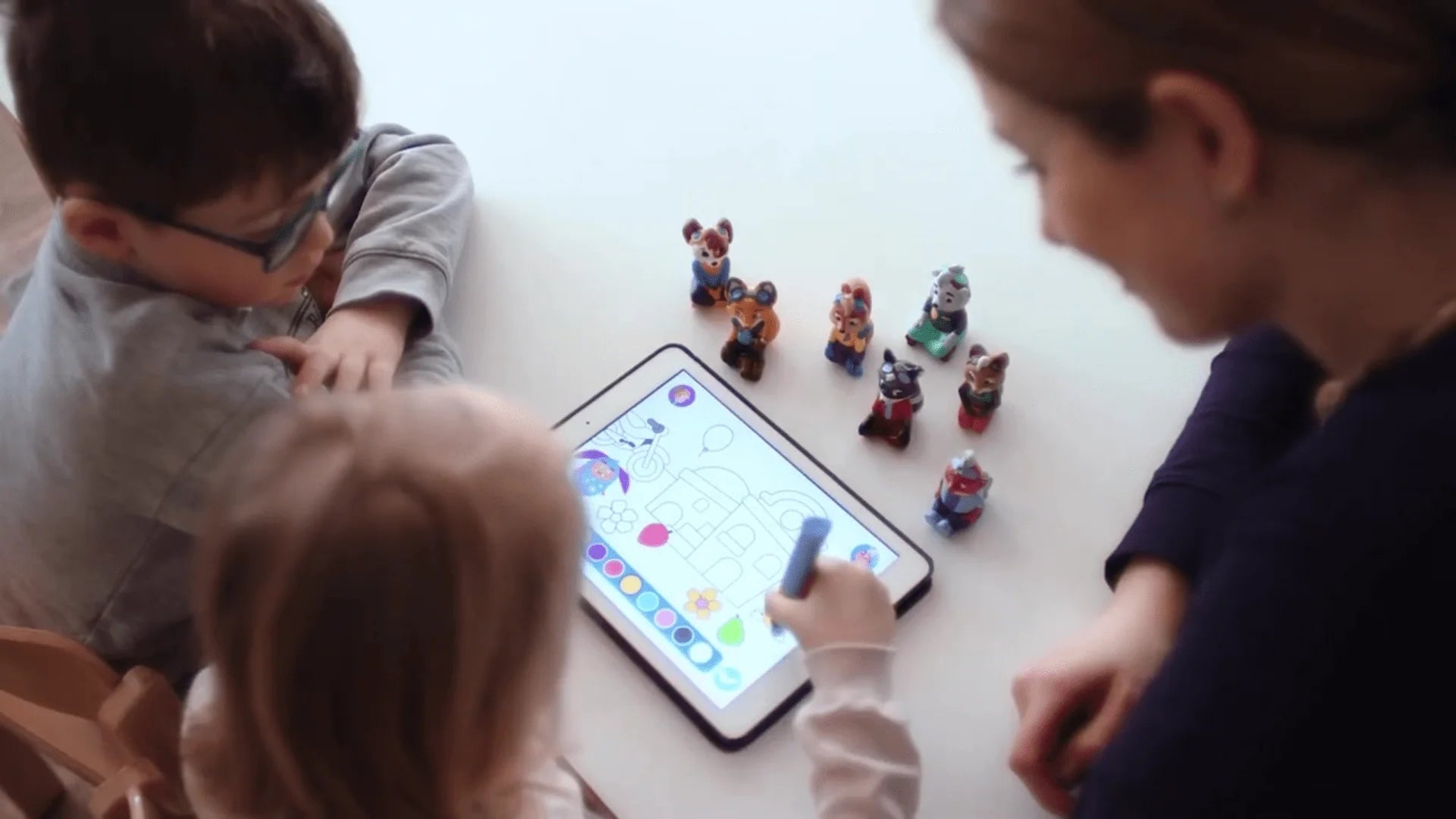 2 Kinder an einem Tablet, betreut von einer Frau, vor ihnen 7 Edurino Figuren.